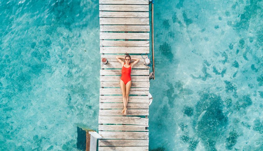 A woman in a red bathing suit lies on a dock surrounded by teal water.